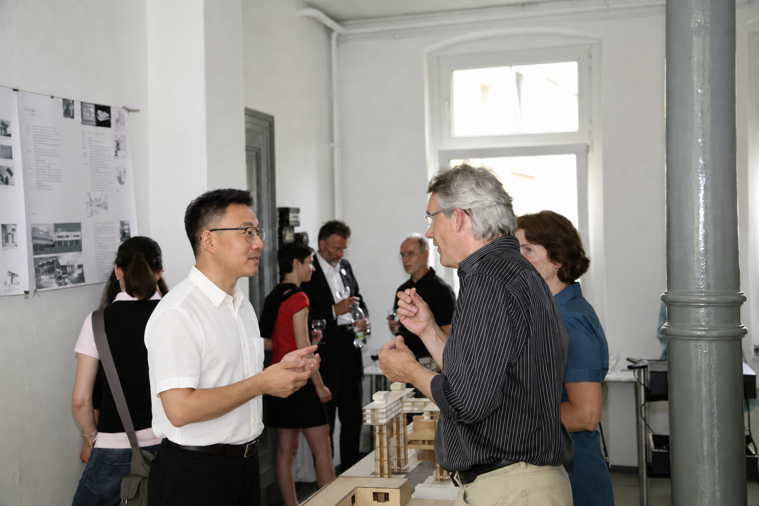 An interior designer speaking with a visitor beside an architectural model.